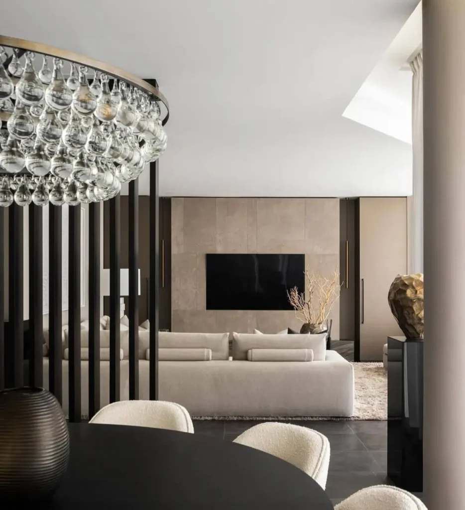 A modern minimalist interior with a slat room divider, a glass bubble chandelier, and a neutral living room in the background.