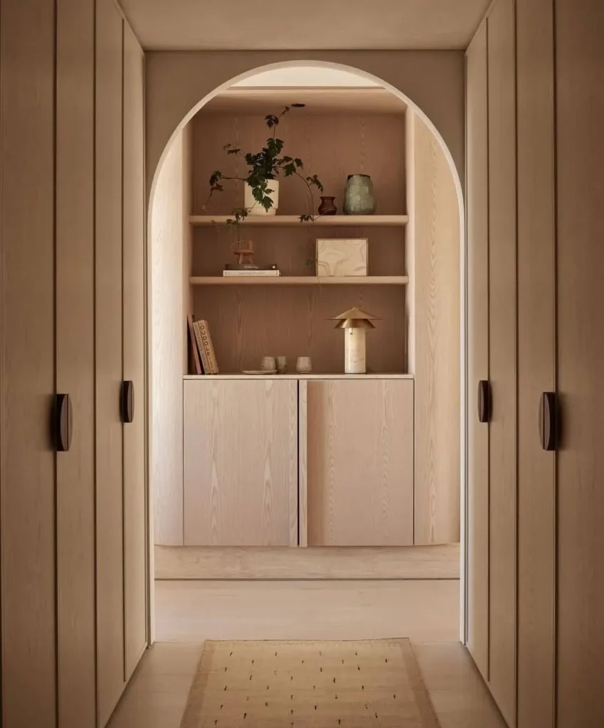 Minimalist hallway with light wood paneling and a view through an arched doorway to a built-in cabinet.