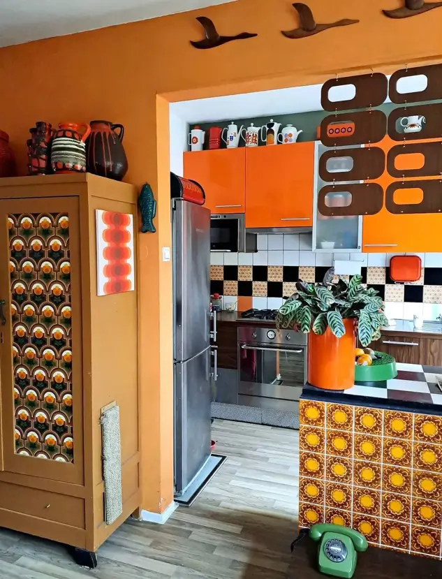 A 70s kitchen with orange cabinets, checkerboard backsplash, and floral tile peninsula, showing 70s interior design ideas.