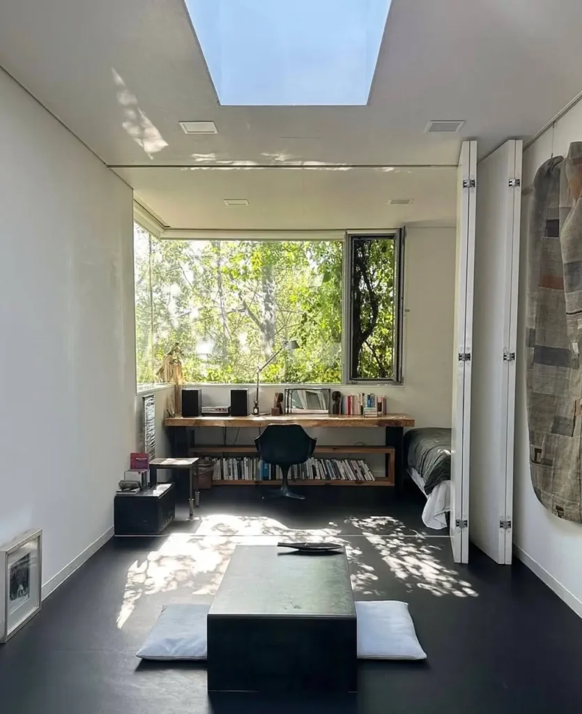 A bright, minimalist small apartment featuring a large window and skylight, showcasing a cozy interior design that maximizes natural light.