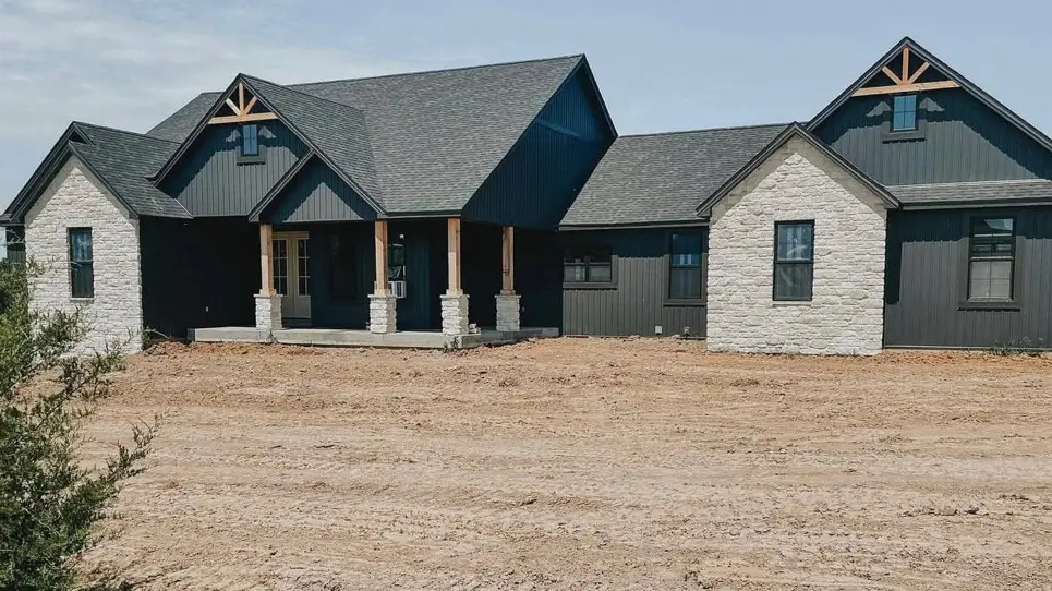 A modern black farmhouse with light stone gables and rustic exposed wood trusses.