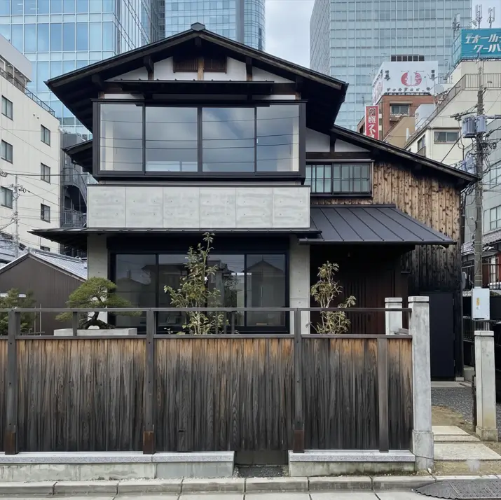 A modern Japanese house exterior with dark wood siding, a concrete beam, and large windows.