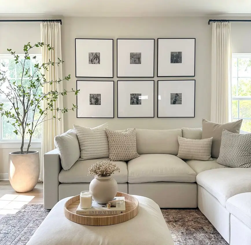 A bright, warm neutral living room with a large off-white sectional and a symmetrical gallery wall of six black-framed pictures.