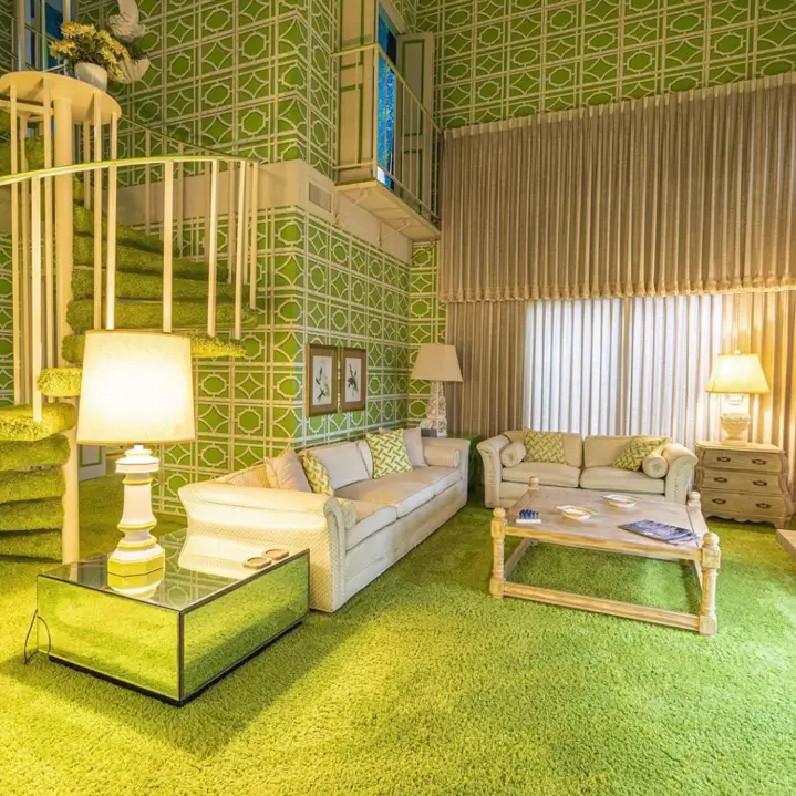 A 70s living room with bright green geometric wallpaper, matching shag carpet, and a spiral staircase.