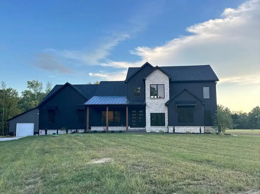 A modern black farmhouse exterior with a prominent light stone accent around the entryway and a dark wood porch.