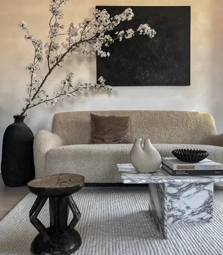 A sophisticated neutral living room with a textured bouclé sofa, a large piece of black wall art, and a marble coffee table.