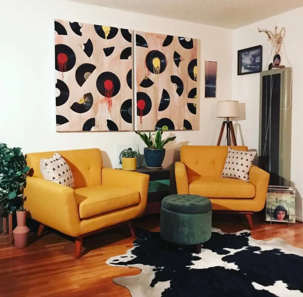 A living room corner with two harvest gold armchairs, a cowhide rug, and vinyl record wall art.