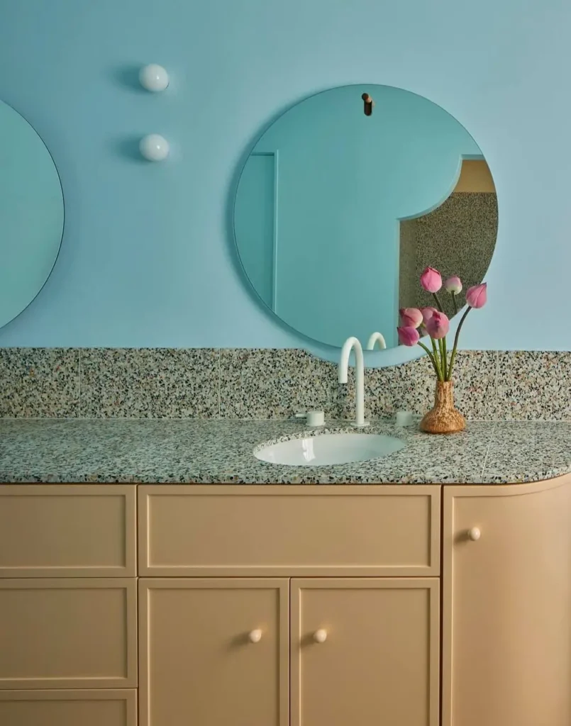 A modern 70s bathroom by AND AND AND STUDIO with a beige vanity, terrazzo countertop, and round globe lights.