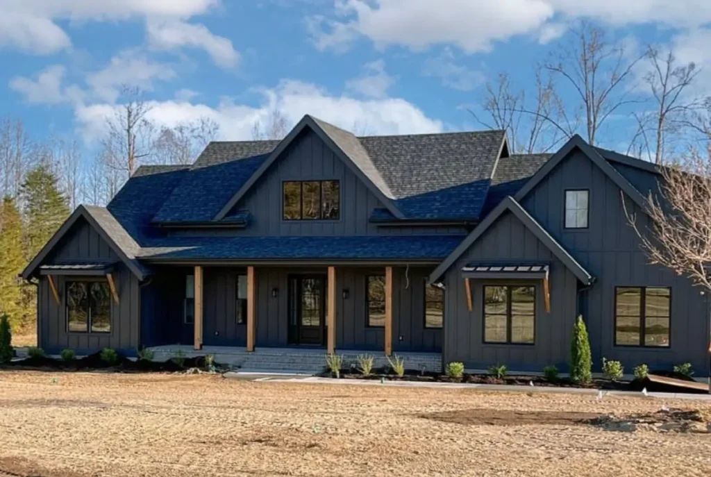 A modern black farmhouse with exposed rustic wood beams supporting the front porch and window awnings.