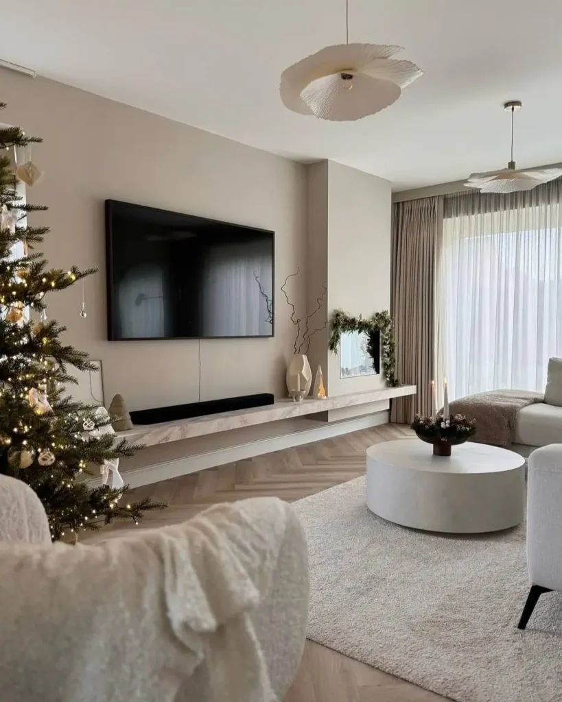 A warm neutral living room featuring greige walls, a floating media console, a round concrete coffee table, and plush white seating.