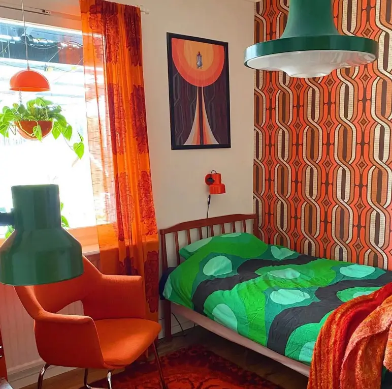 A 70s bedroom inspo room with orange geometric wallpaper, an orange chair, and green accent lighting.