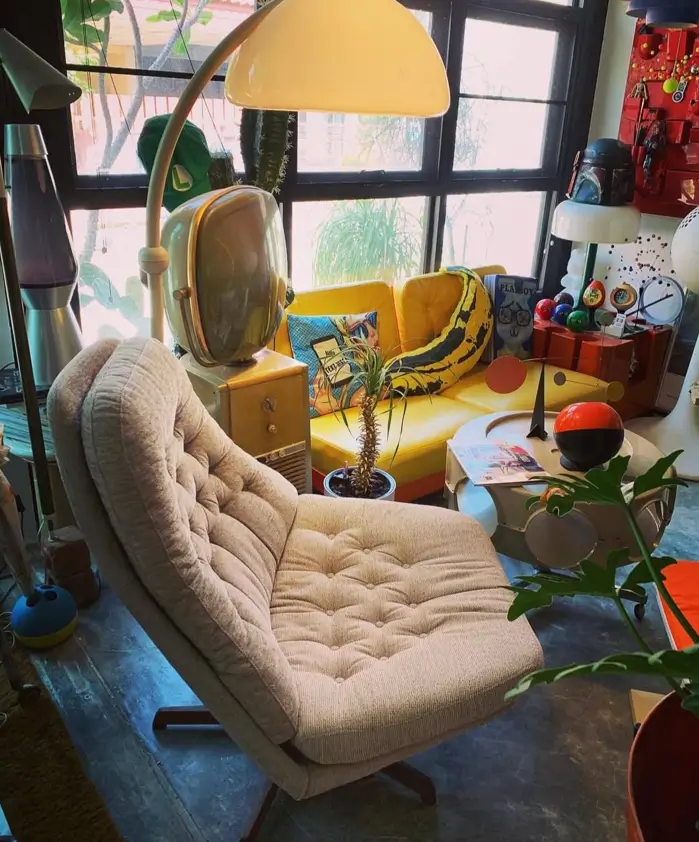 A 70s living room with a tufted swivel chair, a yellow sofa, and an arc lamp.