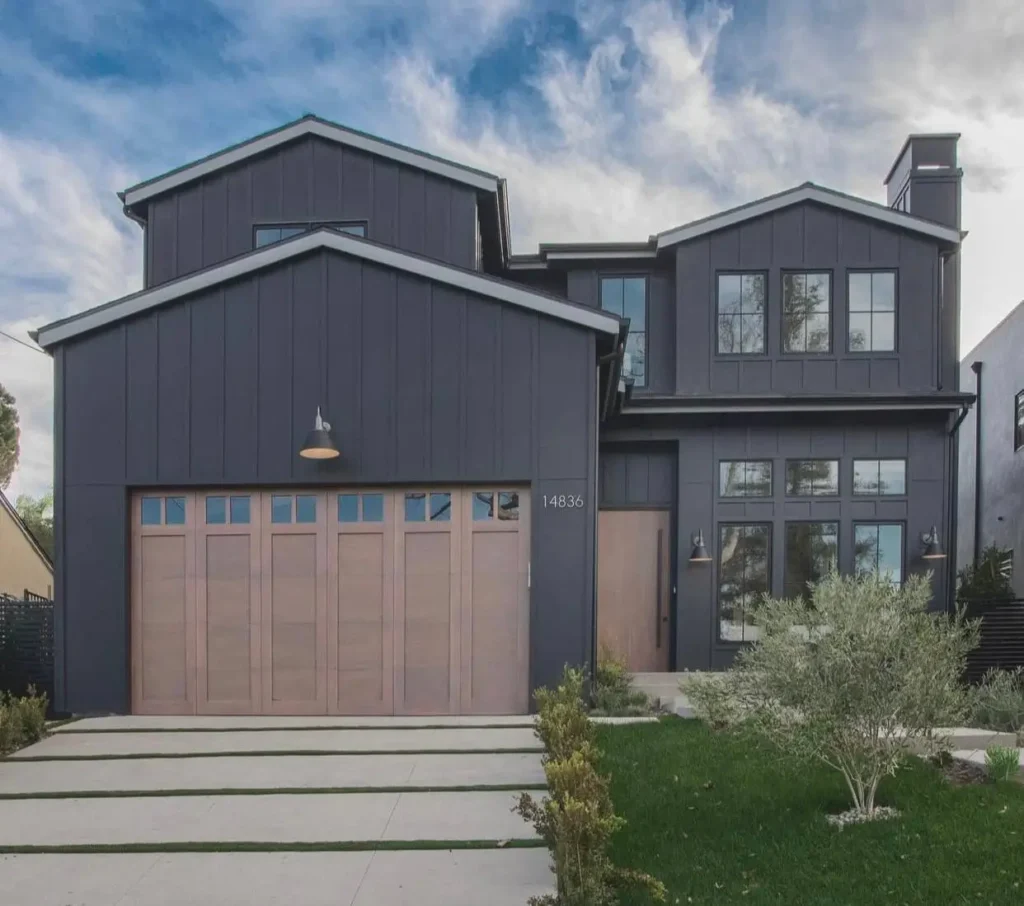 A modern black farmhouse with a light natural wood garage door and matching front door against dark siding.