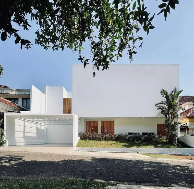 A modern minimalist house with a clean white geometric facade, an open carport, and warm wood slat details.