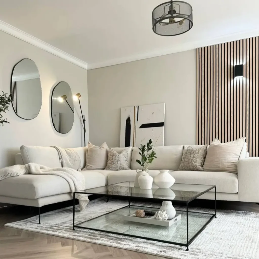 A modern neutral living room with an off-white sectional, a glass coffee table, and a vertical wood slat accent wall.