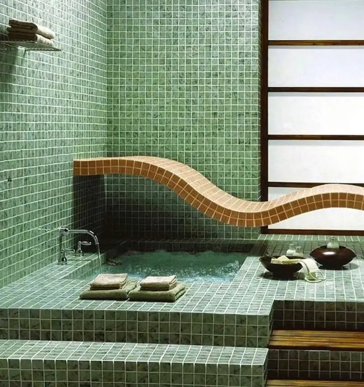 A 70s bathroom featuring a sunken tub and curved bench, all covered in pale green mosaic tile.