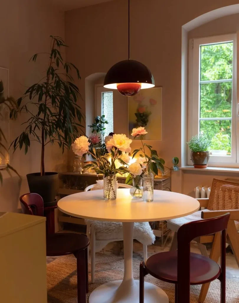 A cozy small apartment dining nook featuring a modern pendant light creating an intimate atmosphere over a white table with peonies.