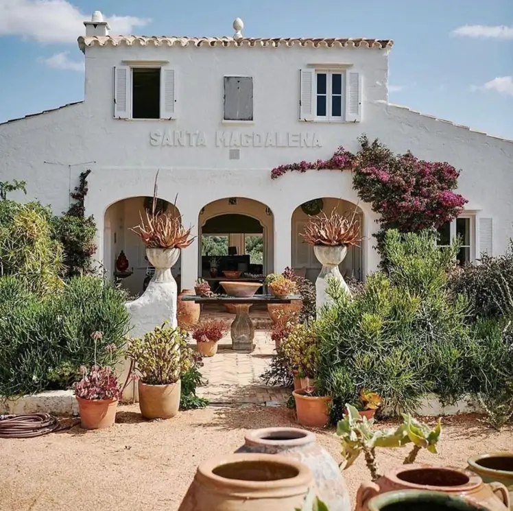 A white stucco Mediterranean house with a triple-arched loggia and a garden full of succulents in terracotta pots.