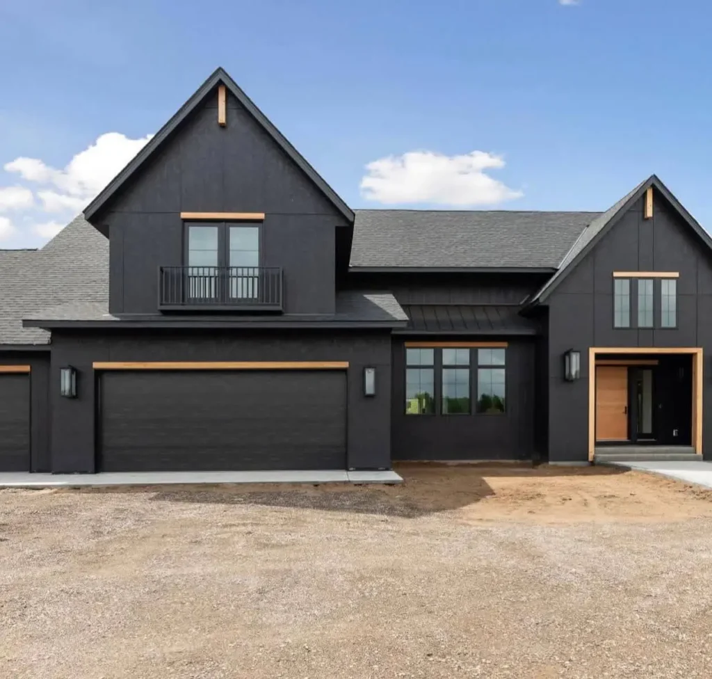 A modern black farmhouse featuring minimal light wood trim that accentuates the gables and a small Juliet balcony.