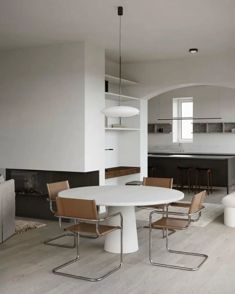 A round white pedestal dining table with tan leather and chrome cantilever chairs in a bright, minimalist open-concept condo.