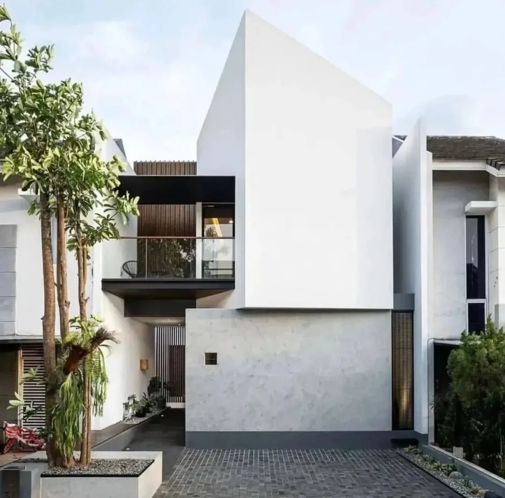 Modern minimalist house with a striking angled white facade over a textured grey base and a recessed balcony.