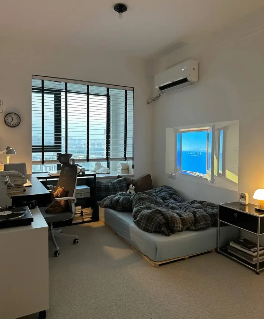 A cozy small apartment bedroom with a projector creating a virtual window view above a plaid-covered bed next to a modern workspace.