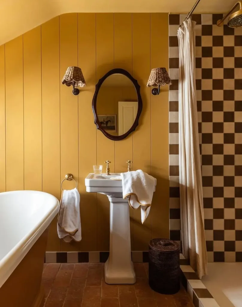 A sophisticated 70s bathroom with harvest gold wood paneling, brown checkerboard shower tile, and rattan wicker sconces.