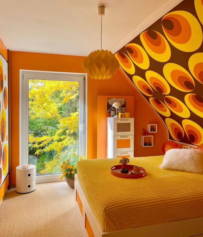 A retro 70s bedroom with bold geometric wallpaper in orange and yellow, and a yellow bedspread.