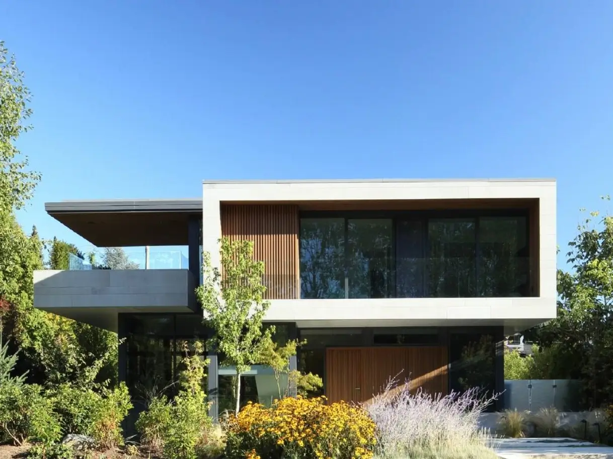 Exterior of a modern minimalist house design featuring a cantilevered upper level, wood accents, and large glass windows, set within a lush garden.