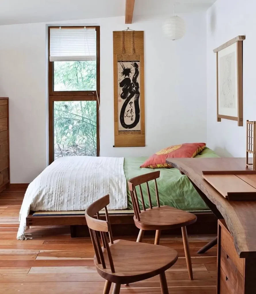 A Japanese-style bedroom with wood floors, a low bed, a live-edge desk, and a calligraphy scroll on the wall.