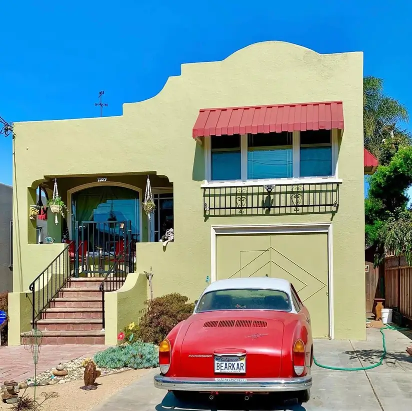 38 Small Mediterranean-Style Homes That Define Coastal Charm 3 Small Mediterranean-style home exterior featuring olive green stucco, a stepped parapet roof, and wrought iron railings.