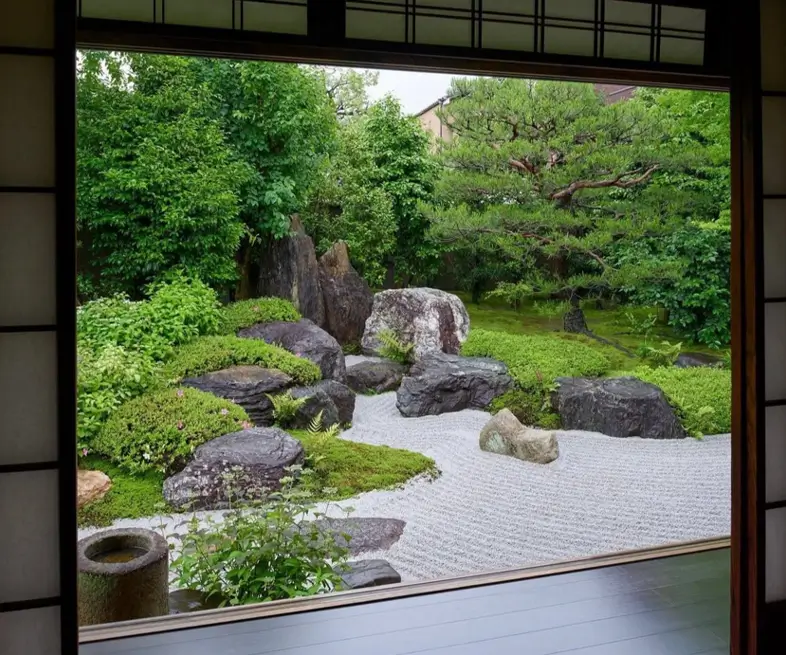 A classic Japanese zen garden with large mossy stones and raked sand, viewed from an interior room.