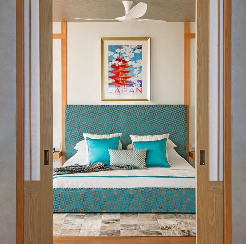 A bedroom viewed through sliding doors, featuring a bright turquoise patterned bed and a vintage Japan travel poster.