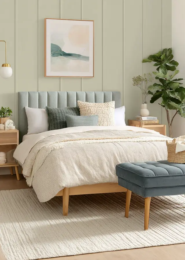 Calm bedroom with pale warm-green vertical paneling, a soft blue-grey headboard, and light wood nightstands.
