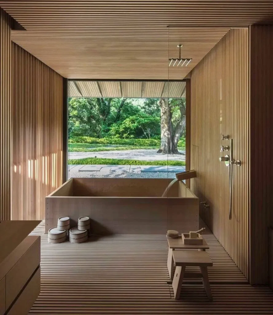 A modern Japanese bathroom with a wooden ofuro soaking tub and a large window looking out onto a Zen garden.