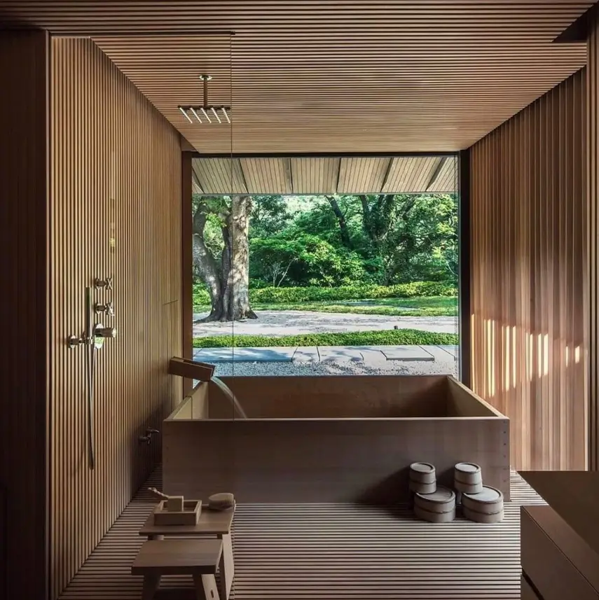 26 Japanese Bathroom Design Ideas for a Serene Home Oasis 14 A Japanese bathroom wet room lined with wood slats, featuring a wooden tub and a large window looking out to a garden.