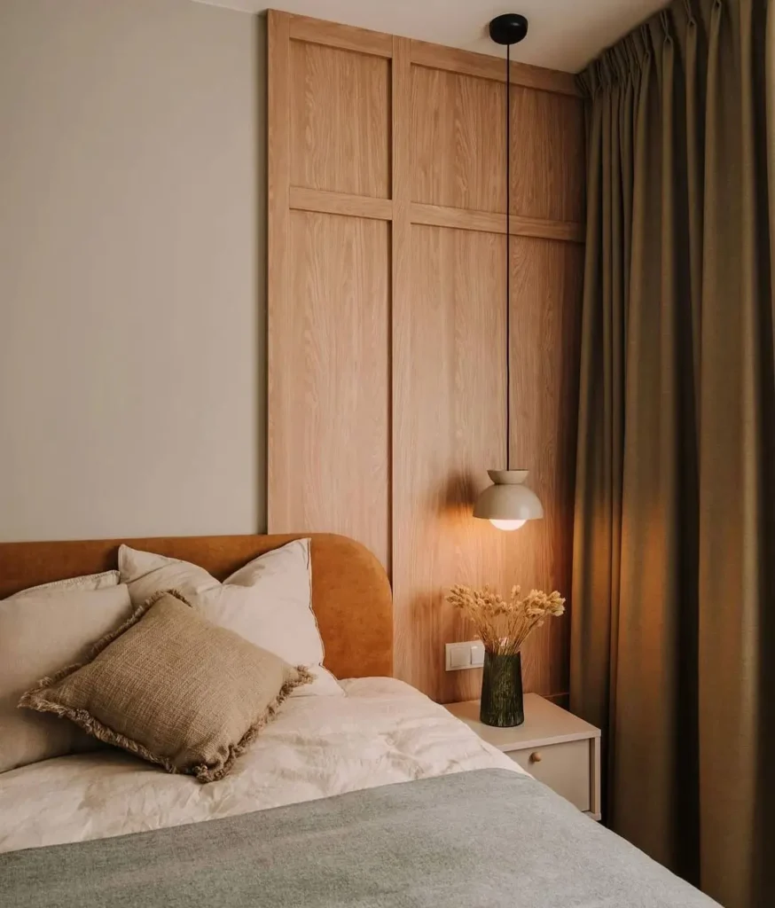 A Japandi bedroom detail with a wood-paneled wall, a rust-colored headboard, and a ceramic pendant light.