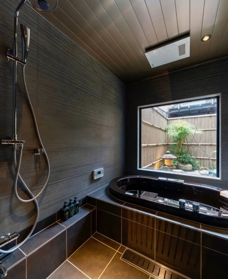26 Japanese Bathroom Design Ideas for a Serene Home Oasis 16 A dark-tiled Japanese bathroom with a soaking tub and a window looking out to a small garden.