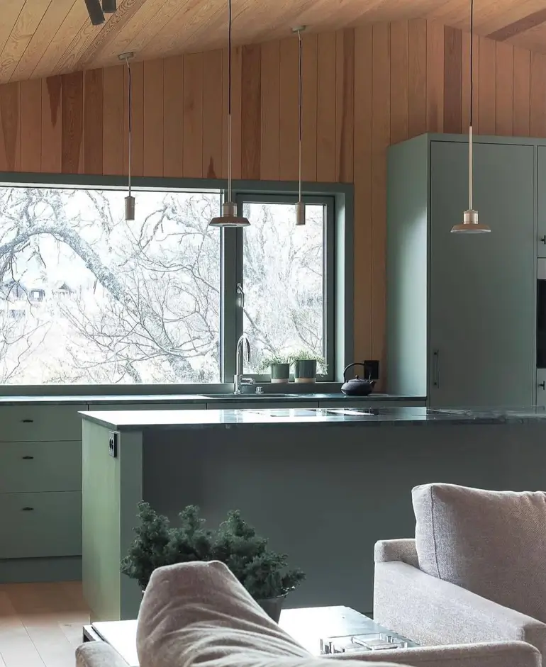 A Japanese inspired kitchen with sage green cabinets, wood paneled walls, and a large window with a view.