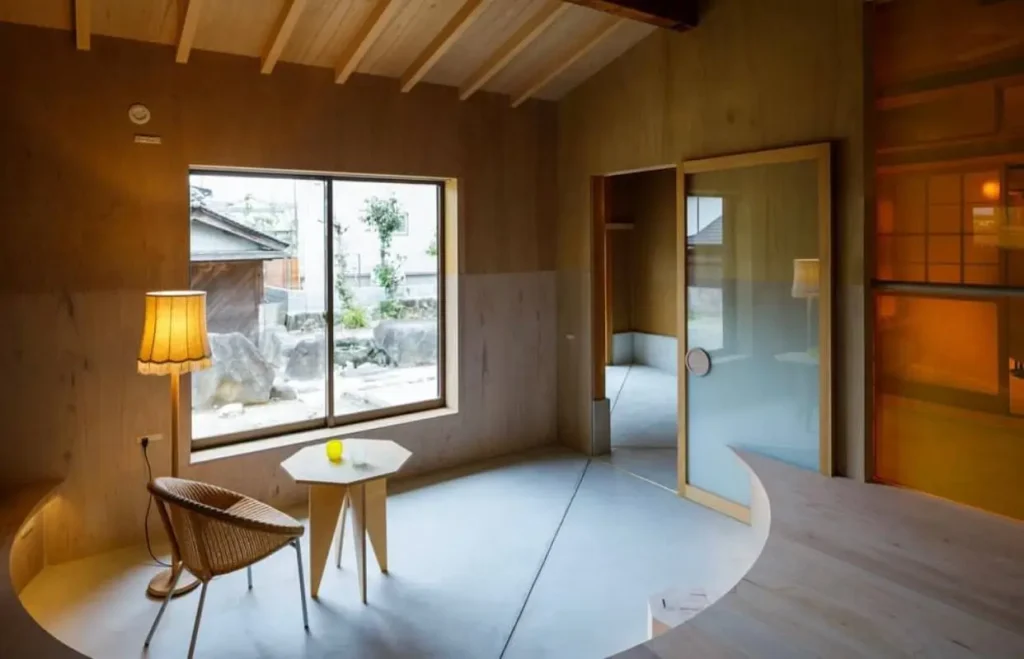 A modern Japanese room with plywood walls, a concrete floor, and a large window overlooking a kare-sansui rock garden.