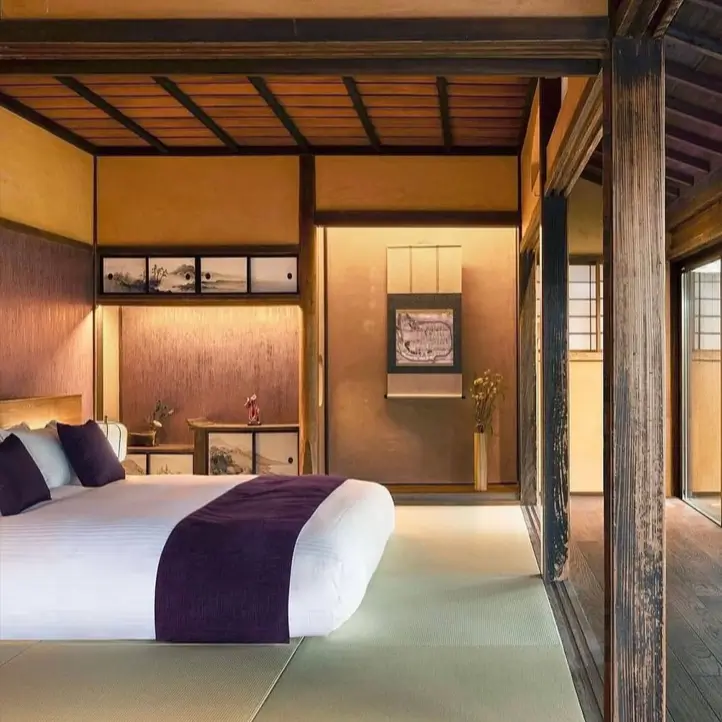 A traditional Japanese bedroom with dark wood beams, tatami floors, and a low modern bed with a purple blanket.