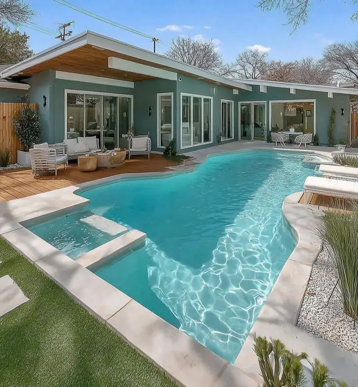 Modern ranch house backyard with blue-gray siding, a wood deck, and a swimming pool.