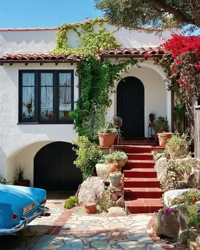 38 Small Mediterranean-Style Homes That Define Coastal Charm 18 White stucco small Mediterranean home with red terracotta steps, large natural rocks, and bright bougainvillea landscaping.