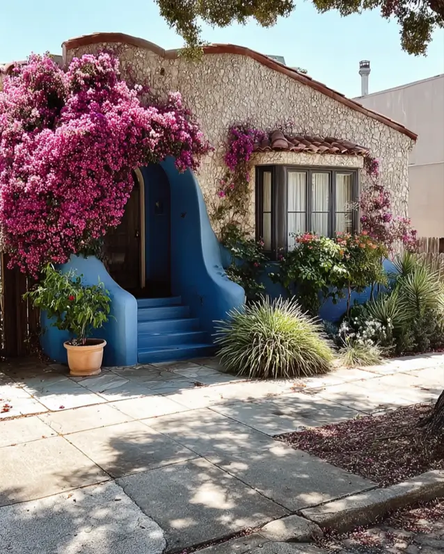 38 Small Mediterranean-Style Homes That Define Coastal Charm 19 Textured stone cottage with a smooth blue arched entryway framed by cascading hot pink bougainvillea.