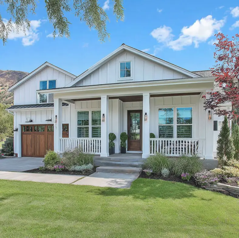 A white modern farmhouse ranch with a front porch and natural wood garage doors.