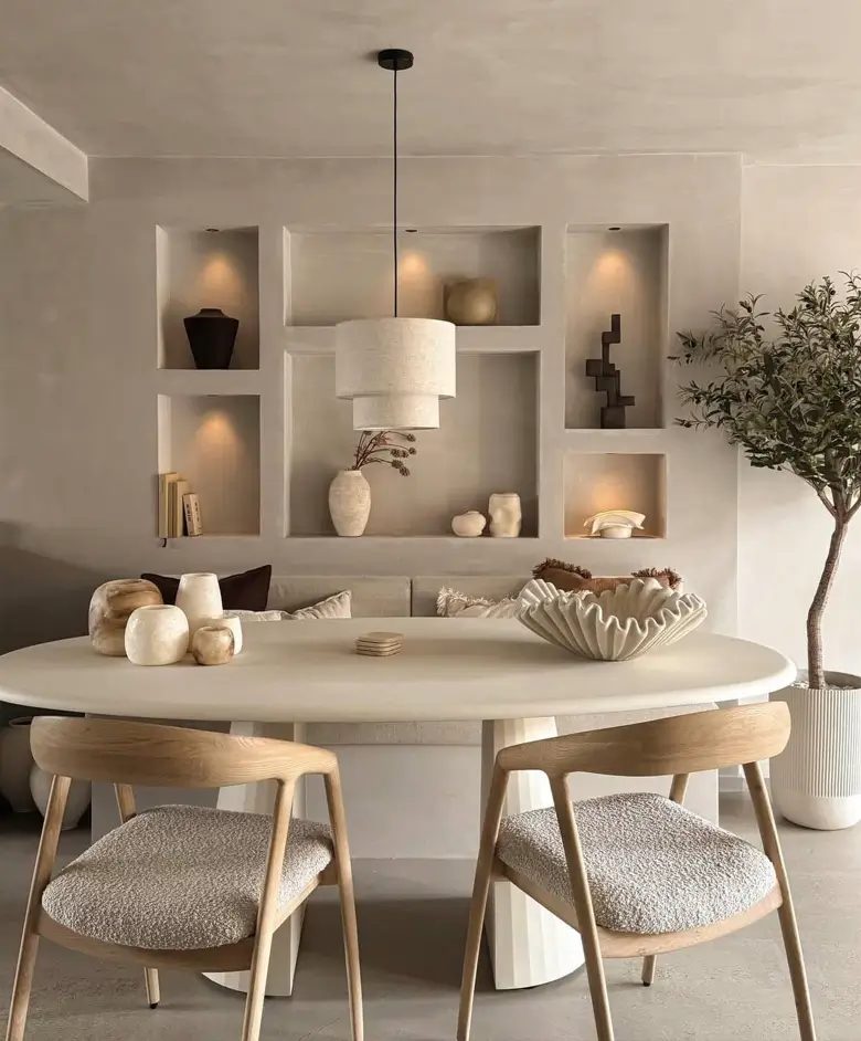 A Japandi dining nook with built-in plaster display niches, an oval table, and light wood chairs.