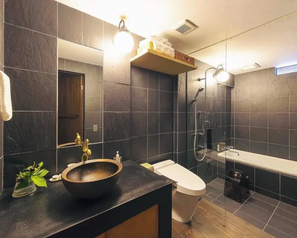 26 Japanese Bathroom Design Ideas for a Serene Home Oasis 20 A Japanese inspired bathroom with dark slate tiles, a bronze vessel sink, and a modern white toilet.
