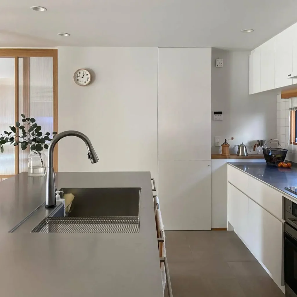 A minimal Japanese style kitchen with white cabinets and a large stainless steel island workstation.