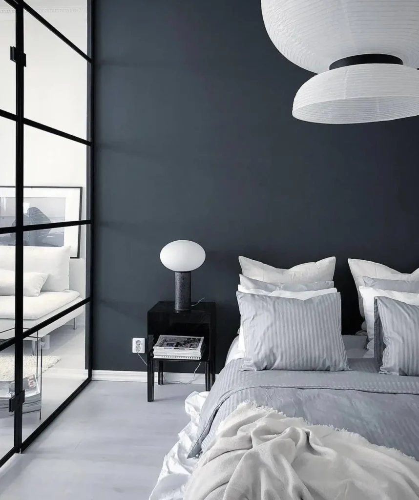 A modern dark-walled bedroom featuring large white paper lanterns and a black-framed glass partition.