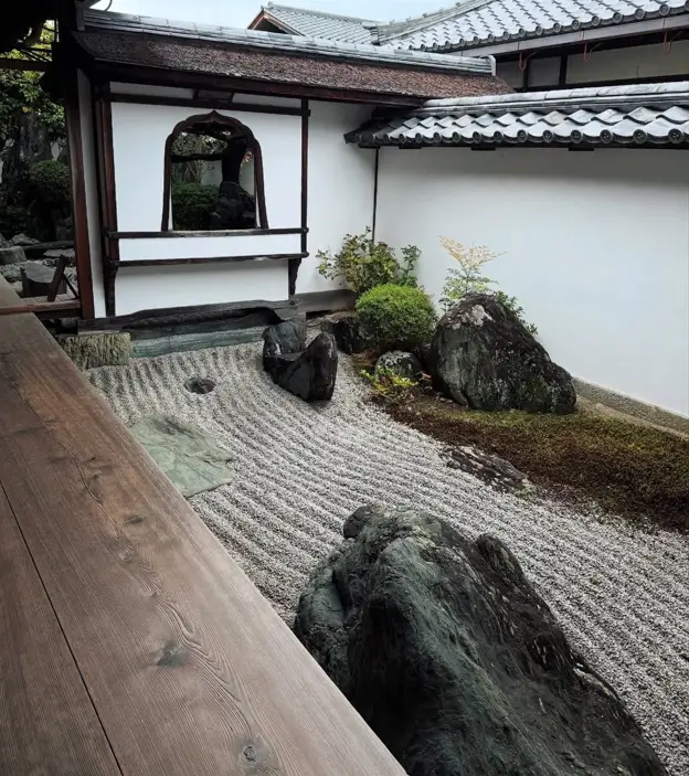 Raked gravel zen garden with a bell-shaped window looking onto another garden.